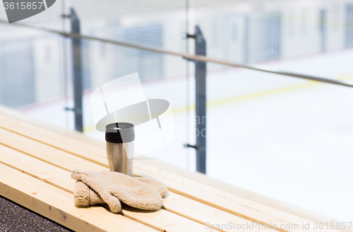Image of thermos cup and mittens on bench at ice rink arena