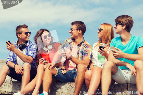Image of group of smiling friends with smartphones outdoors