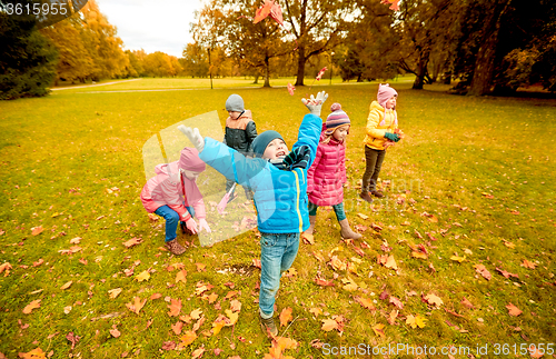Image of happy children playing with autumn leaves in park