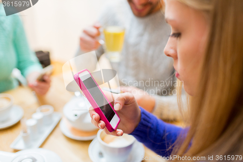 Image of woman with friends texting on smartphone at cafe