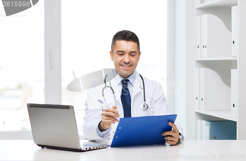 Image of happy doctor with clipboard and laptop in office