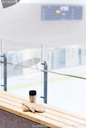 Image of thermos cup and mittens on bench at ice rink arena