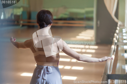 Image of classic ballet dancer posing at barre on rehearsal room background