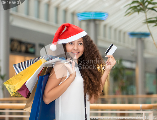 Image of Christmas shopping, girl holding colorful shopping bags wearing santa hat 