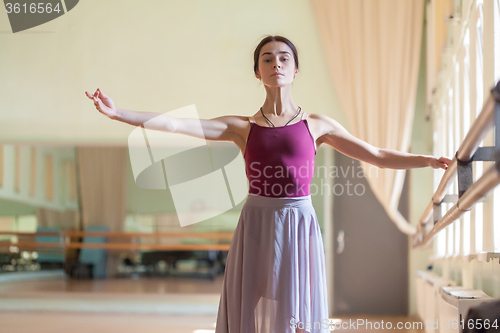 Image of classic ballet dancer posing at barre on rehearsal room background