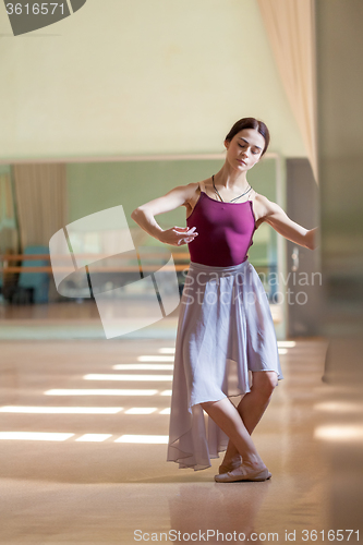 Image of classic ballet dancer posing at barre on rehearsal room background