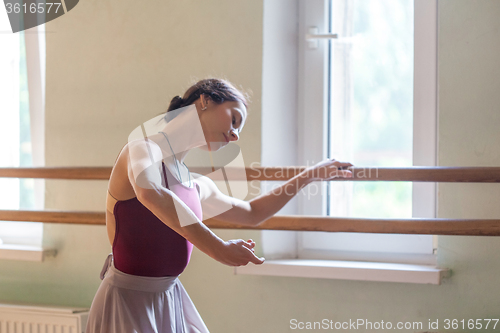 Image of classic ballet dancer posing at barre on rehearsal room background