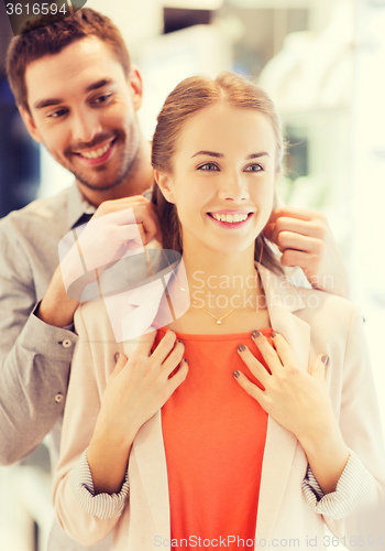 Image of couple trying golden pendant on at jewelry store
