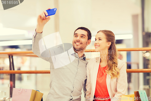 Image of happy couple with smartphone taking selfie in mall