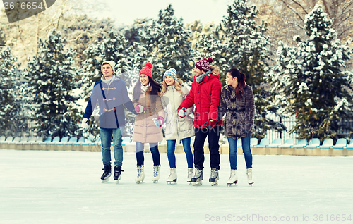 Image of happy friends ice skating on rink outdoors