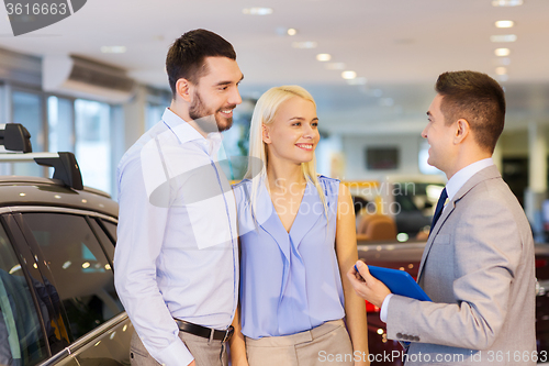 Image of happy couple with car dealer in auto show or salon