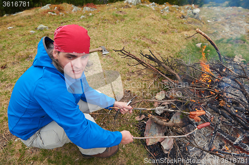 Image of hiking man prepare tasty sausages on campfire