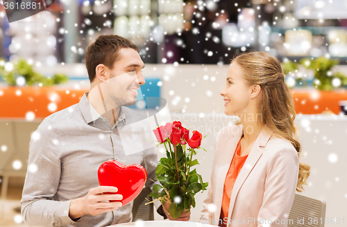 Image of happy couple with present and flowers in mall