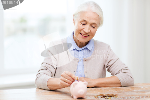 Image of senior woman putting money to piggy bank at home