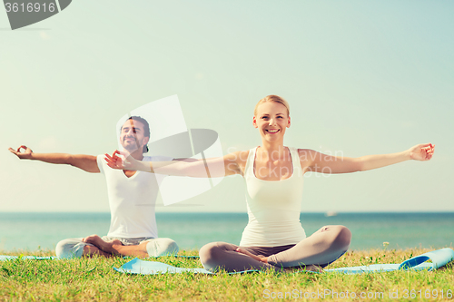 Image of smiling couple making yoga exercises outdoors