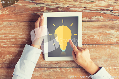 Image of close up of hands with lighting bulb on tablet pc