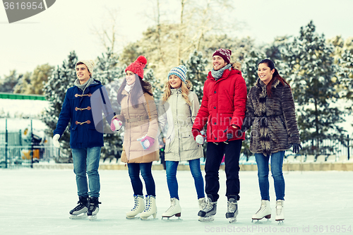 Image of happy friends ice skating on rink outdoors