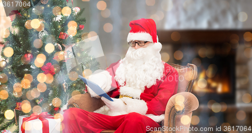 Image of santa claus with tablet pc in armchair at home