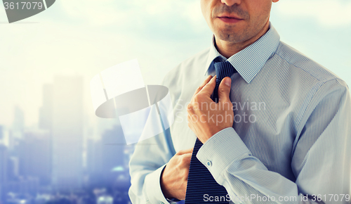 Image of close up of man in shirt adjusting tie on neck