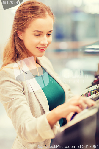 Image of happy young woman choosing clothes in mall