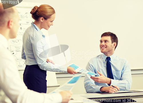 Image of smiling woman giving papers to man in office