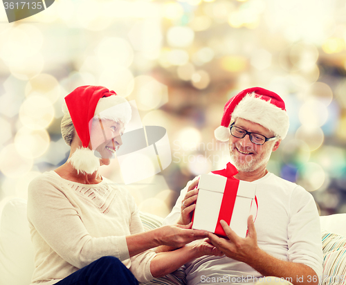 Image of happy senior couple in santa hats with gift box