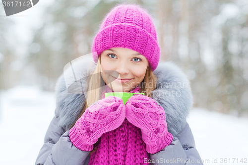 Image of smiling young woman with cup in winter forest