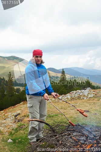 Image of hiking man prepare tasty sausages on campfire