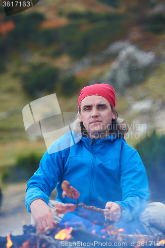 Image of hiking man prepare tasty sausages on campfire