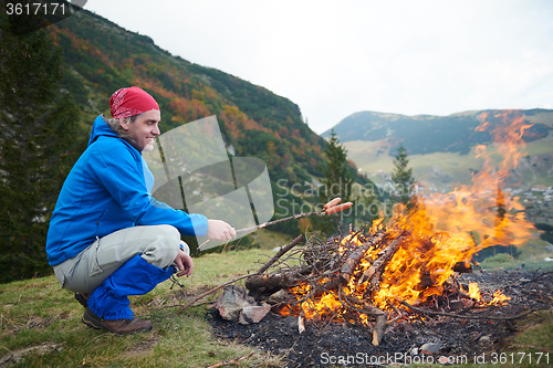 Image of hiking man prepare tasty sausages on campfire