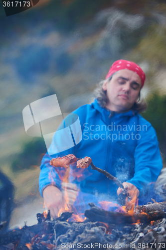 Image of hiking man prepare tasty sausages on campfire