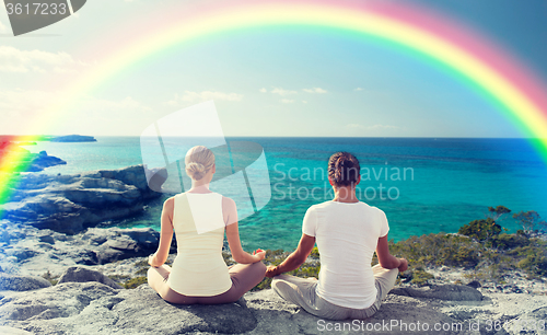 Image of happy couple meditating in lotus pose on beach