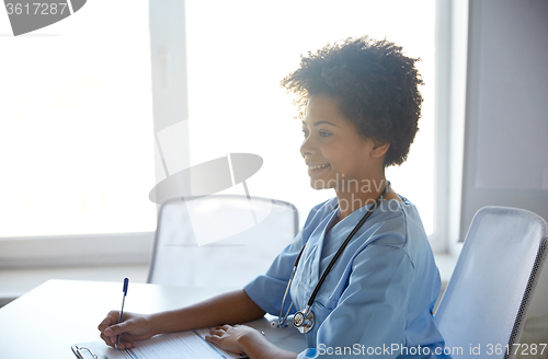 Image of happy female doctor or nurse writing at hospital