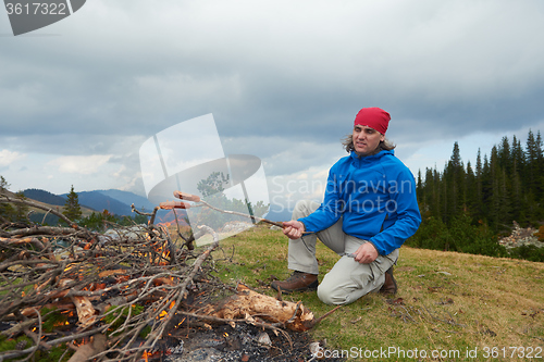 Image of hiking man prepare tasty sausages on campfire