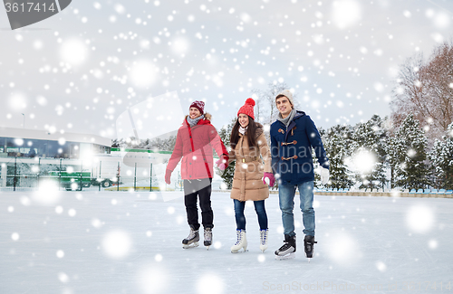 Image of happy friends ice skating on rink outdoors