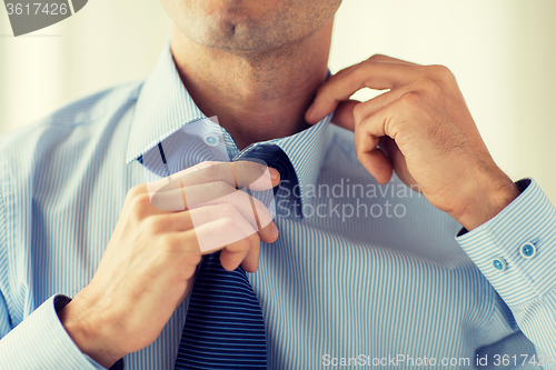 Image of close up of man in shirt adjusting tie on neck