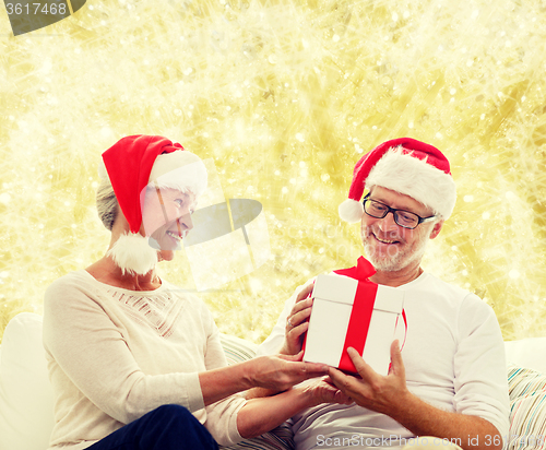 Image of happy senior couple in santa hats with gift box