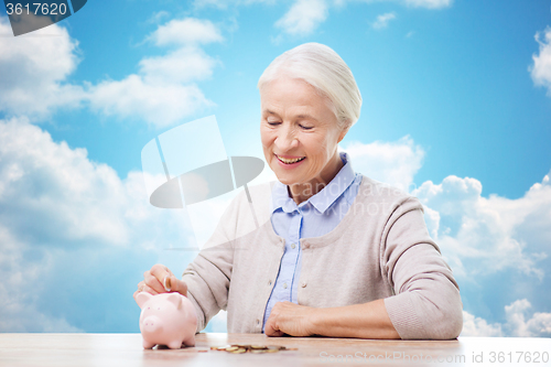 Image of senior woman putting money to piggy bank