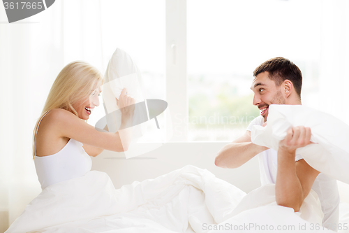 Image of happy couple having pillow fight in bed at home