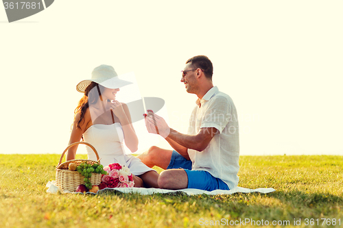Image of smiling couple with small red gift box on picnic