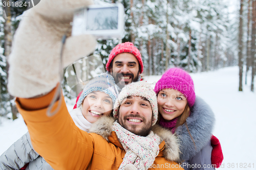 Image of smiling friends with camera in winter forest