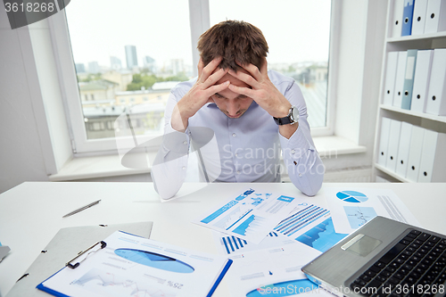 Image of stressed businessman with papers in office