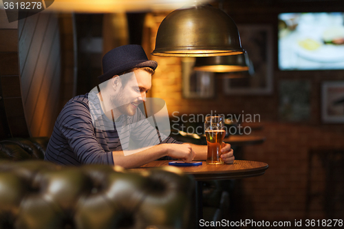 Image of man with smartphone and beer texting at bar