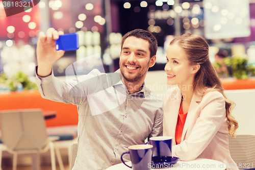 Image of happy couple with smartphone taking selfie in mall