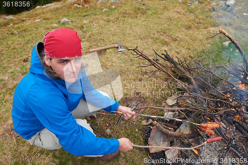 Image of hiking man prepare tasty sausages on campfire