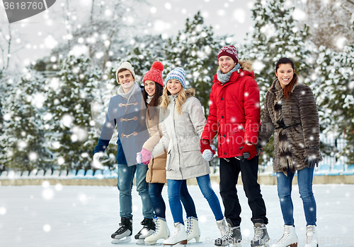 Image of happy friends ice skating on rink outdoors