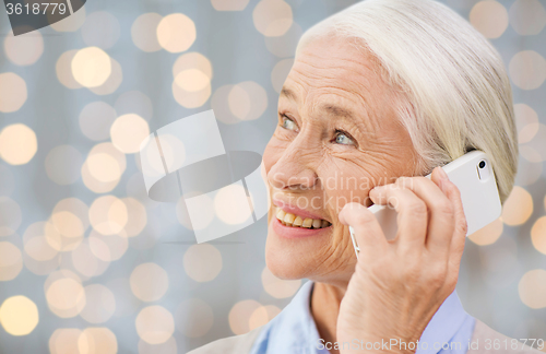 Image of senior woman with smartphone calling over lights