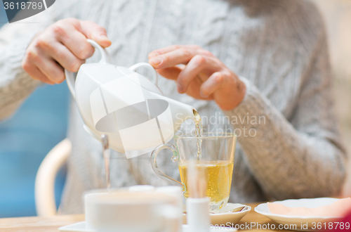 Image of close up of man with pot pouring tea at cafe