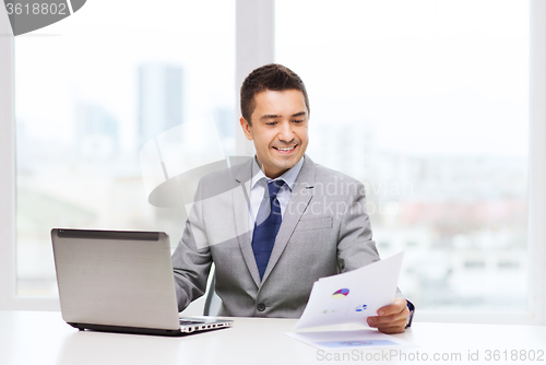 Image of smiling businessman with laptop and papers