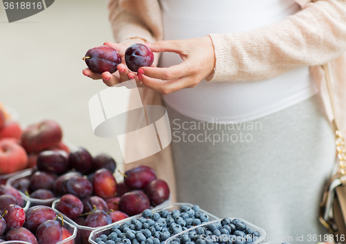 Image of pregnant woman choosing plums at street market